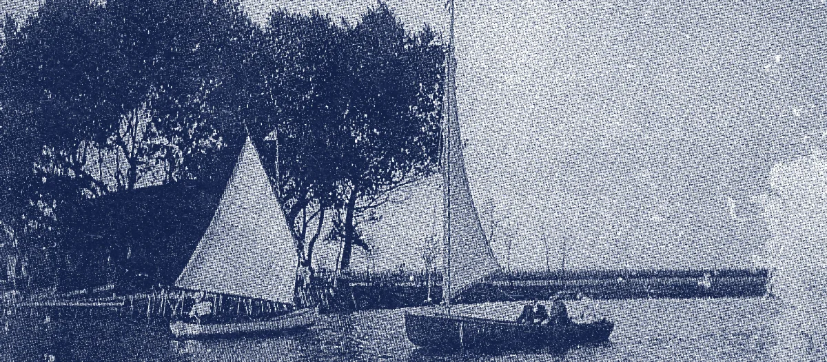 Historic photo showing two small sailboats on calm water in front of a row of trees – early Fassmer-built boats around 1910, marking the transition from traditional craftsmanship to modern boatbuilding.