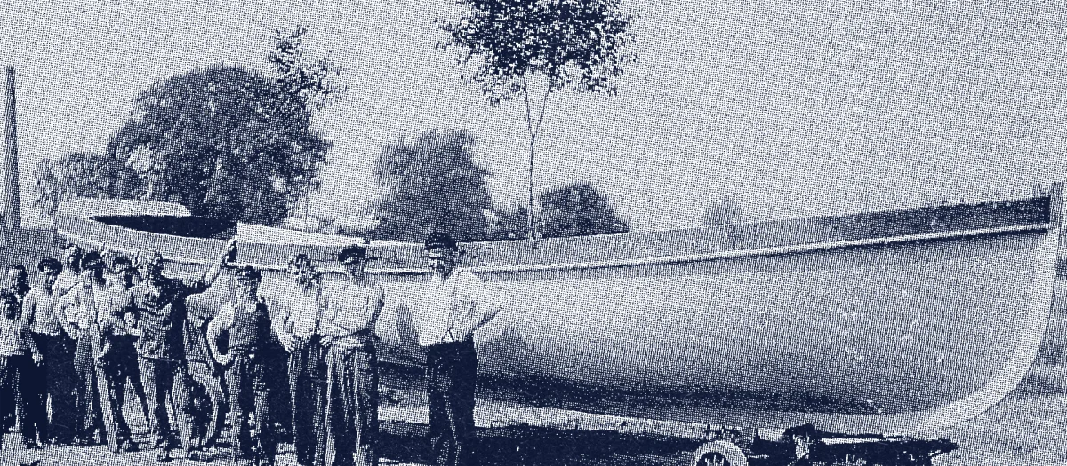 Historic black-and-white photo of Fassmer employees around 1940 at the launching of a large wooden boat; shipyard workers pose in front of the vessel on a transport wagon, with a decorated tree marking the successful completion.