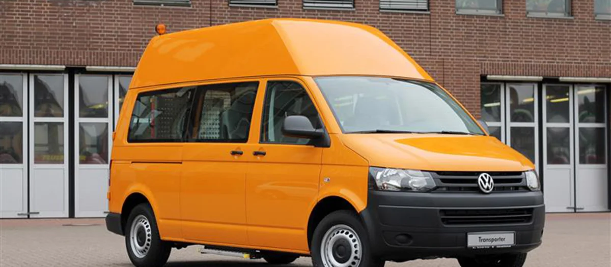 An orange Volkswagen Transporter with a high roof on company premises. Fassmer Automotive manufactures the lightweight, durable GRP high roof used in vehicle construction.