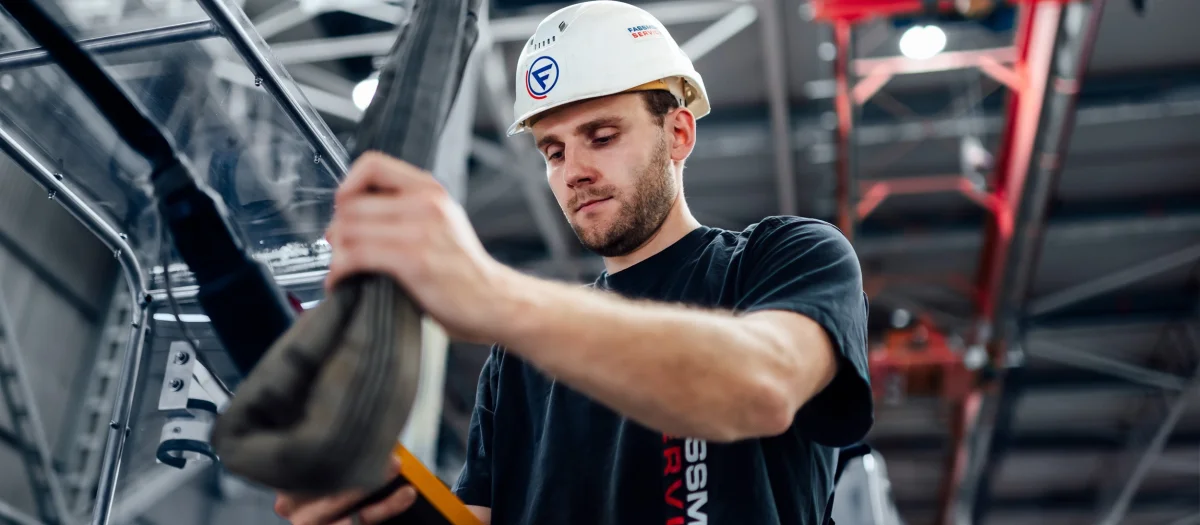 Fassmer Service employee at work in the shipyard: young man with safety helmet and Fassmer logo working focused on a component.