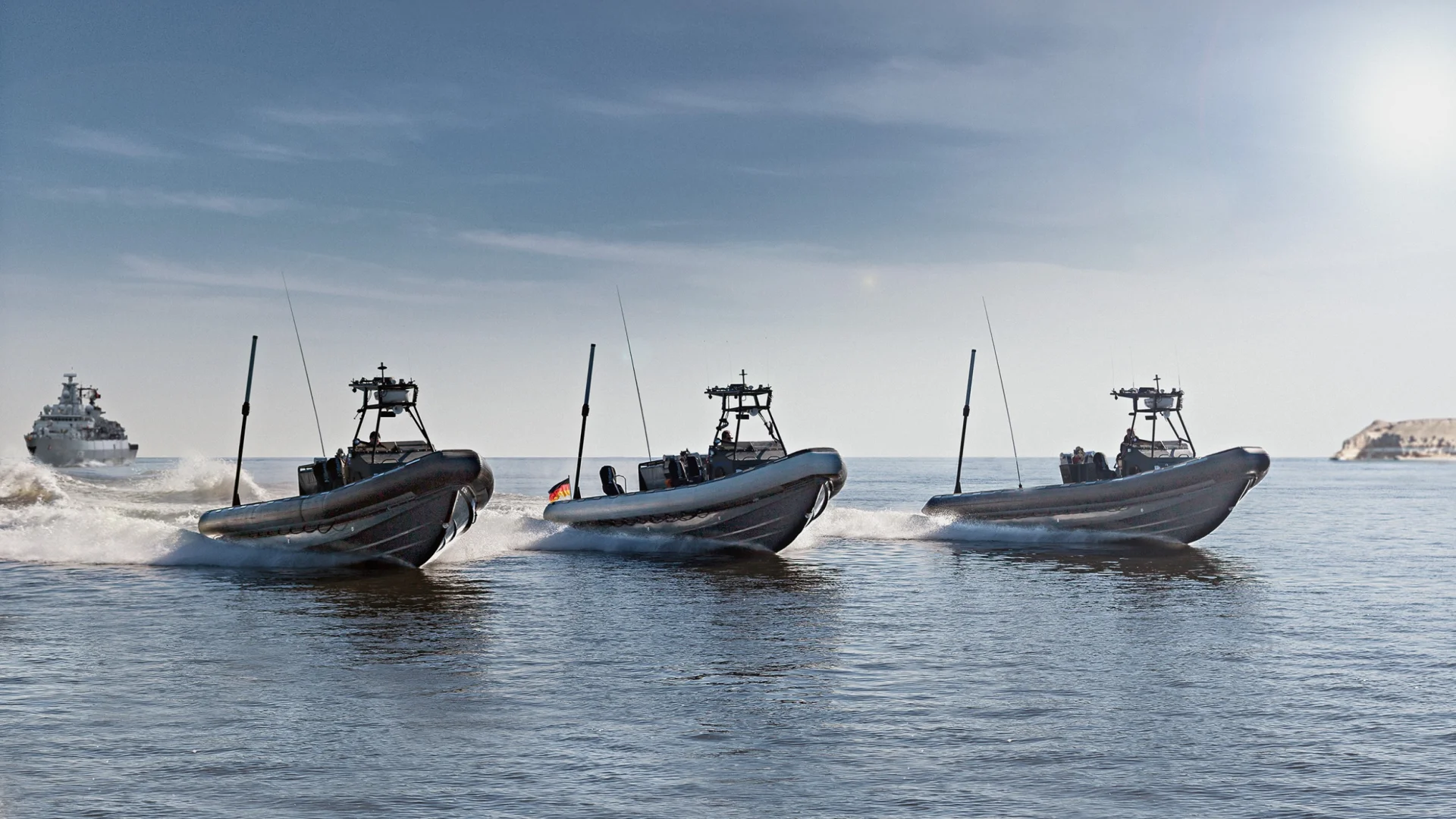 Three military RIB fast boats by Fassmer Defence at high-speed operation, navy vessel in background