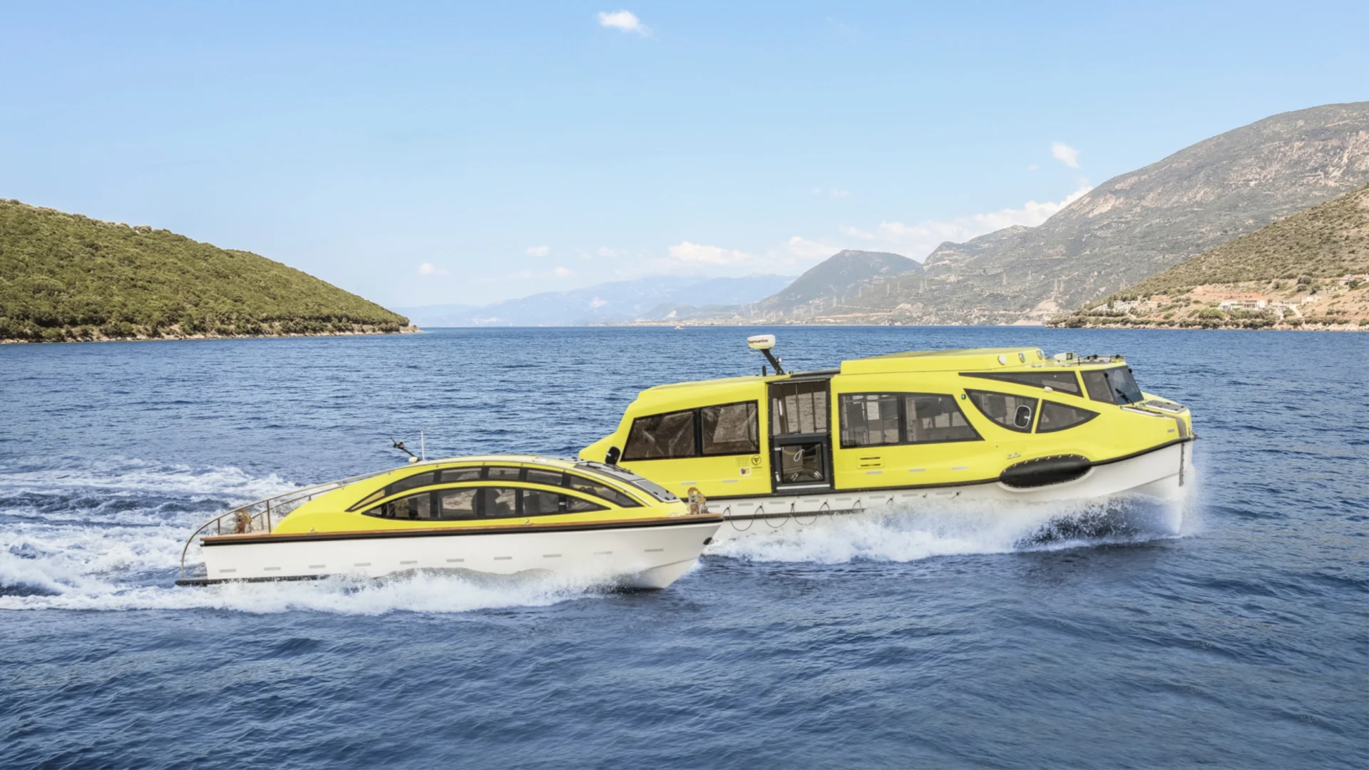 Two yellow Fassmer tender boats sailing side by side on the sea, surrounded by green hills and coastal landscape. The modern vessels serve as tenders and lifeboats for cruise ships.