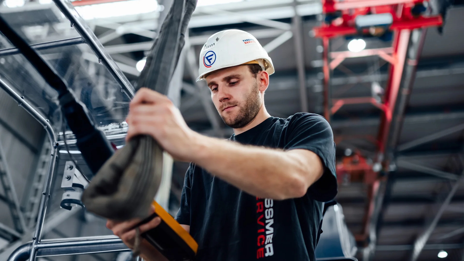 Fassmer Service employee at work in the shipyard: young man with safety helmet and Fassmer logo working focused on a component.