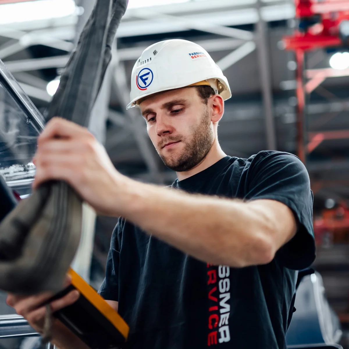 Fassmer Service employee at work in the shipyard: young man with safety helmet and Fassmer logo working focused on a component.