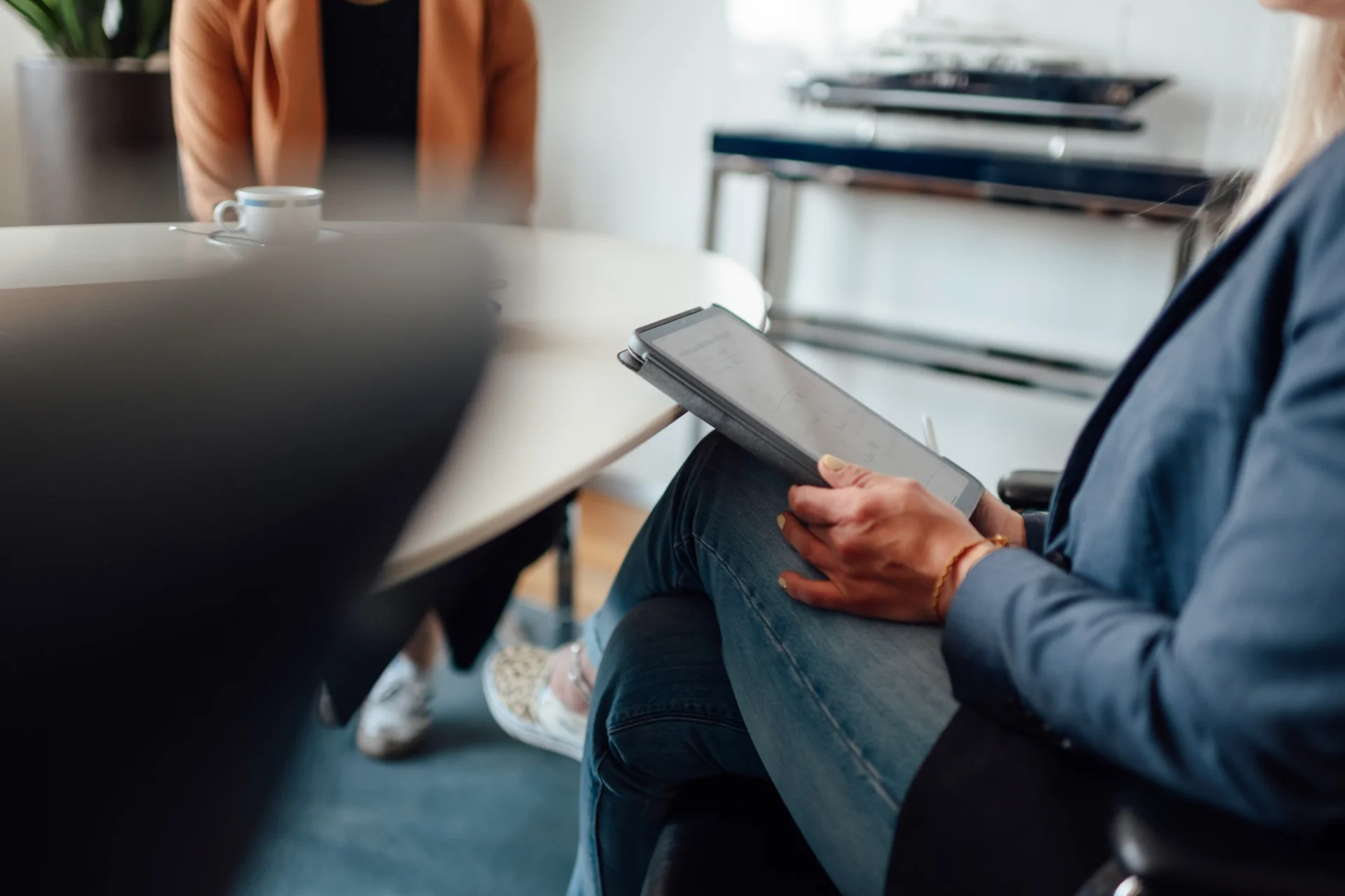 Job interview at Fassmer: A smiling employee in a light green shirt sits in a modern office with plants, talking to a candidate. Careers and jobs in shipbuilding.