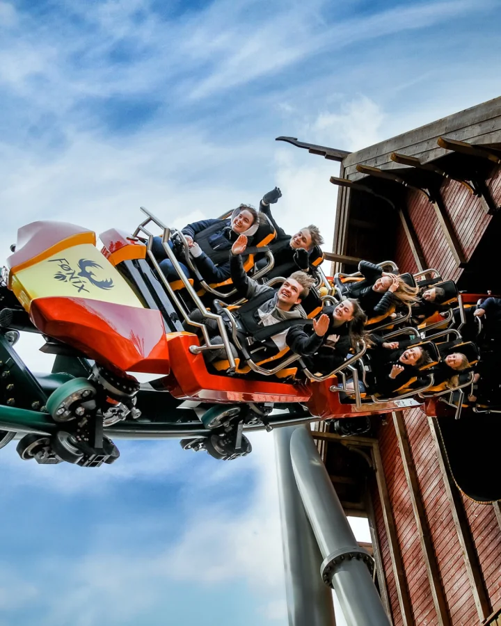 People riding the “Fønix” roller coaster at Fårup Sommerland in Denmark. The train emerges from a wooden building as passengers raise their arms. The lightweight composite components were manufactured by Fassmer, a specialist in composite solutions for the leisure industry.