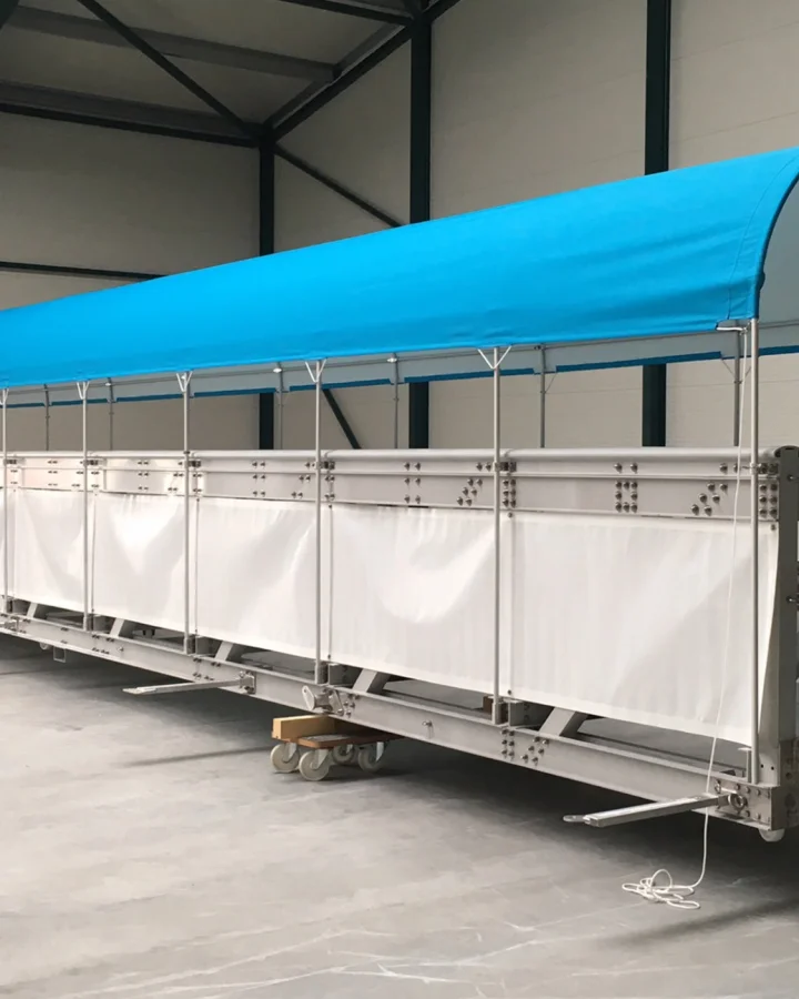 A covered aluminum gangway with a light blue canopy and side panels inside a workshop. The gangway is a Fassmer in-house development designed to ensure safe and weather-protected passenger access to ships or offshore platforms.