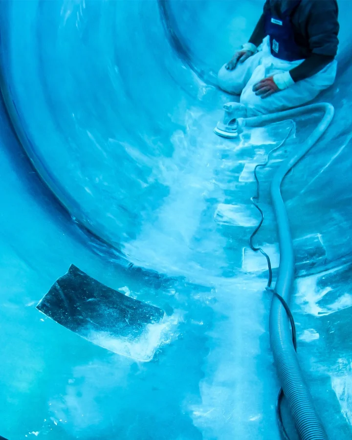 A person working inside a large blue fiberglass-reinforced plastic (FRP) tube, likely during repair or maintenance. The image shows surface treatment with a hose system – illustrating Fassmer’s composite expertise in the repair and maintenance of fiber-reinforced structures.