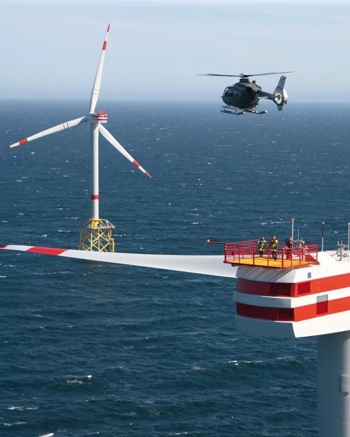 Offshore wind turbine with helicopter above the nacelle where people are standing. The scene depicts a modern wind power installation at sea.