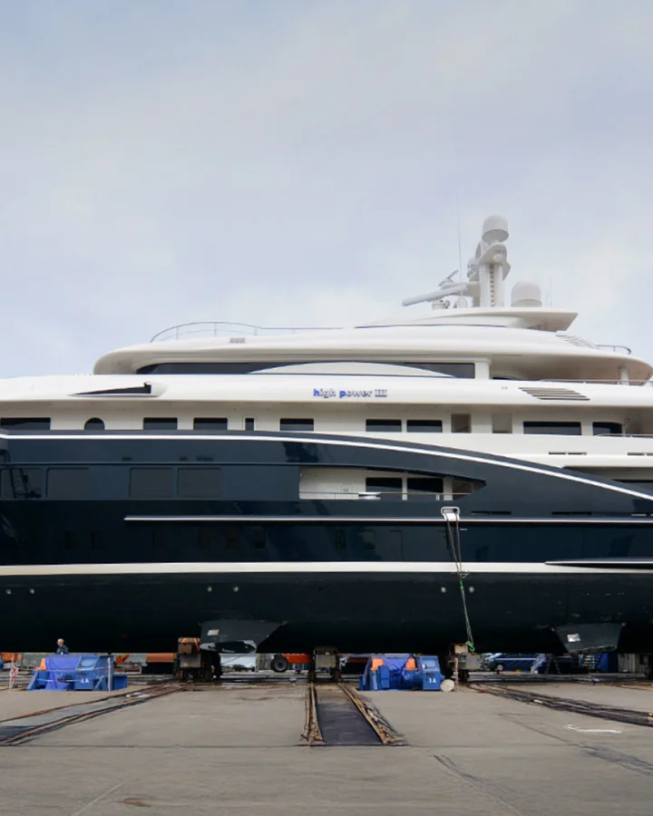 The luxury yacht High Power III dry-docked in a shipyard area, prepared for maintenance; side view showing sleek lines and multiple decks.