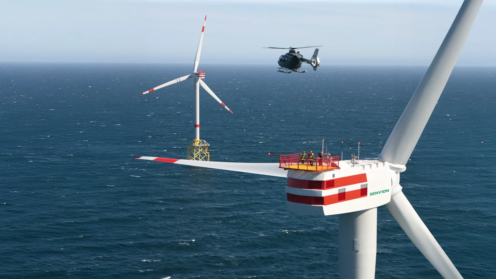 Offshore wind turbine with helicopter above the nacelle where people are standing. The scene depicts a modern wind power installation at sea.